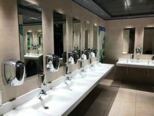 Foto di un bagno pubblico con cinque lavandini sulla sinistra, con ognuno il suo specchio e i dispenser di sapone. 