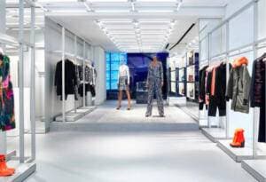 Foto di un negozio di abbigliamento. Ai lati ci sono abiti appesi e scarpe appoggiate sotto. Al centro due manichini. 