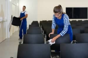 Foto di due operatori che puliscono e sistemano delle poltroncine di una sala riunioni