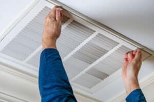 Immagine ravvicinata di due mani che smontano la griglia di un condotto di areazione posto sul soffitto