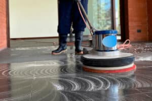 Immagine ravvicinata di un operatore che usa una monospazzola per lavare un pavimento in marmo. 