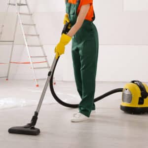 Operatore che aspira con aspirapolvere una stanza appena ristrutturata vuota con all'interno solo una scala. 